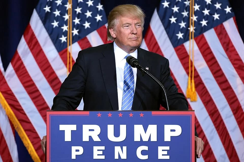 Donald Trump speaking at a campaign podium reading "Trump Pence"